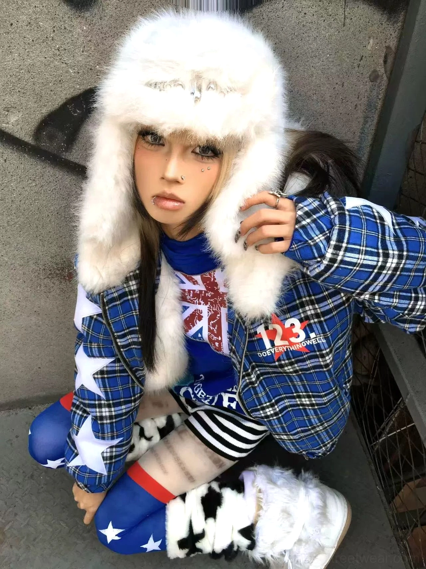 Blue plaid star puffer jacket with oversized white star appliques, faux-fur-lined hood, and graphic chest print styled in an urban streetwear setting