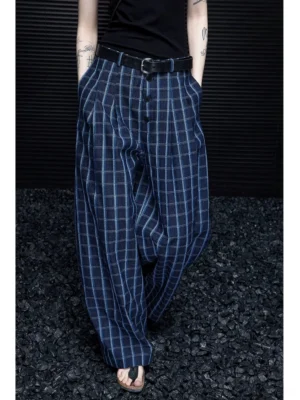 Blue plaid wide-leg streetwear trousers shown in a low-angle view with a dark navy windowpane pattern, pleated waist, black belt styling, and full-length flowing legs