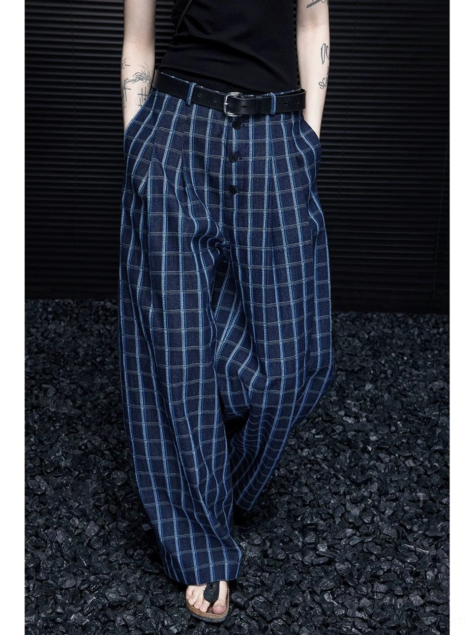 Blue plaid wide-leg streetwear trousers shown in a low-angle view with a dark navy windowpane pattern, pleated waist, black belt styling, and full-length flowing legs