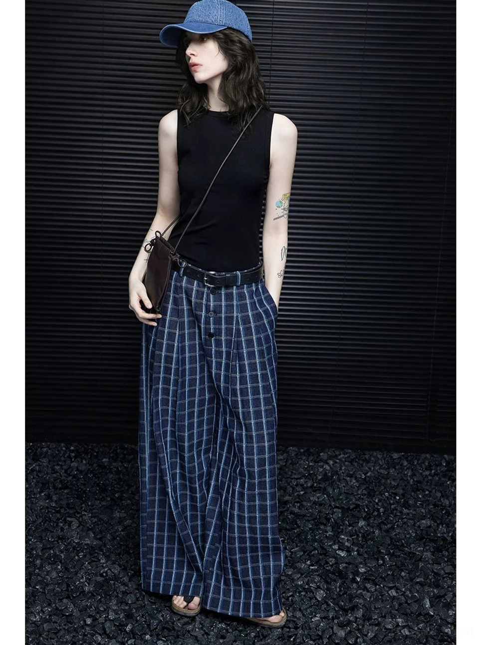Women wearing loose blue plaid wide-leg trousers in side profile with a crossbody bag, black belt, fitted top, and flat sandals
