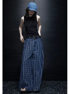 Women wearing blue plaid wide-leg trousers in a full-body front view with a pleated waistband, black tank top, leather belt, and open-toe sandals