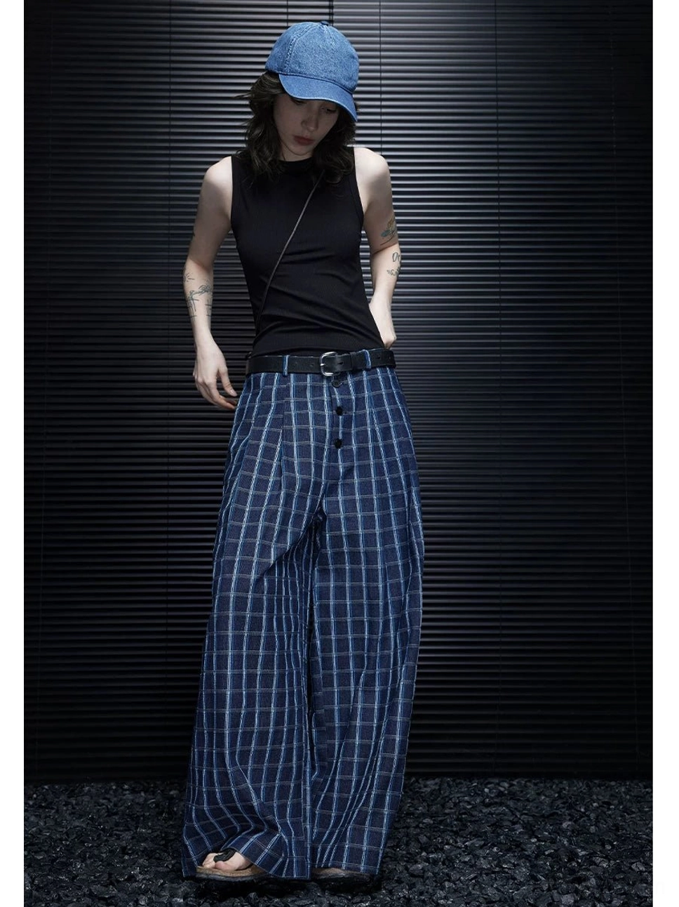 Women wearing blue plaid wide-leg trousers in a full-body front view with a pleated waistband, black tank top, leather belt, and open-toe sandals