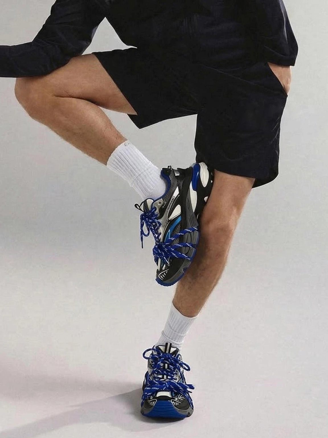 Blue retro athletic dad sneakers worn by a male model with black loungewear, featuring bold blue laces and a futuristic chunky sole