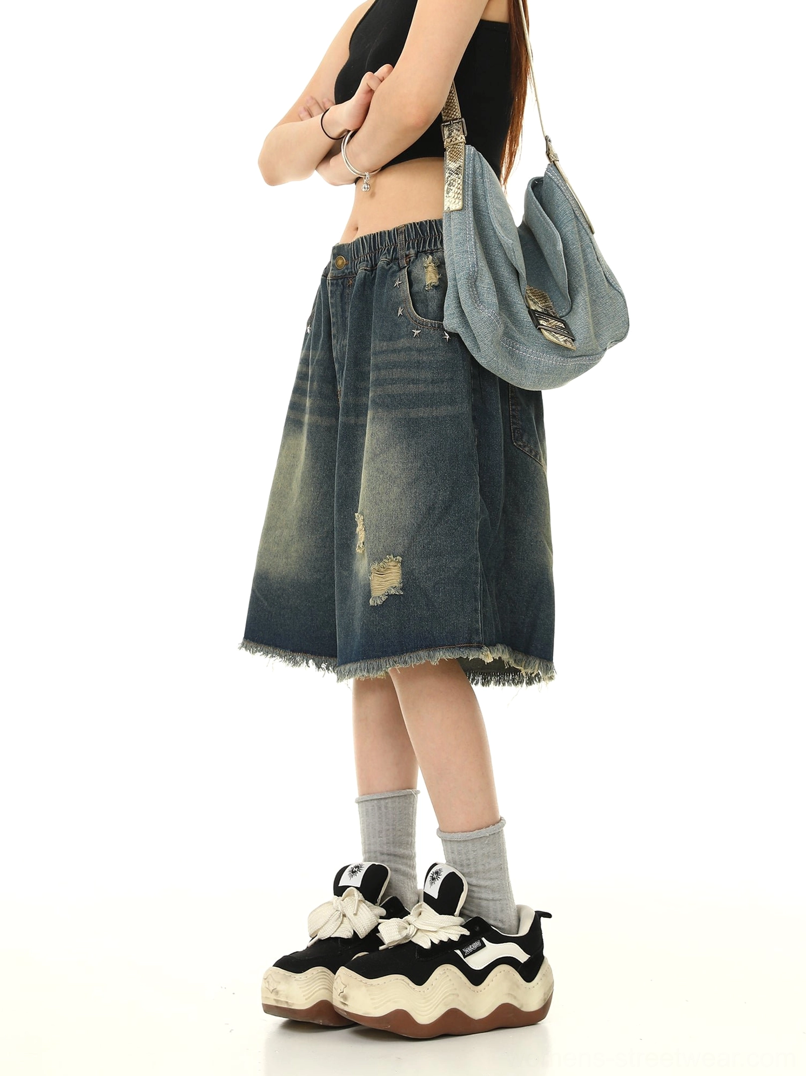 Left-side streetwear view of blue ripped denim Bermuda shorts featuring distressed patches, a loose silhouette, and frayed raw hem