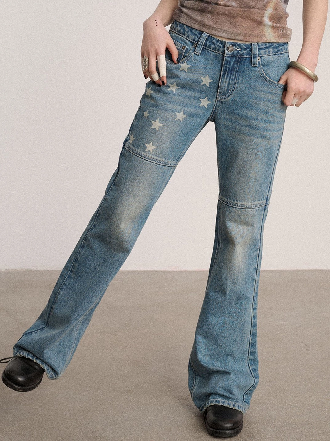 Dynamic side front view of blue star print flared jeans with faded denim texture, knee seams, graphic upper legs, and wide hems