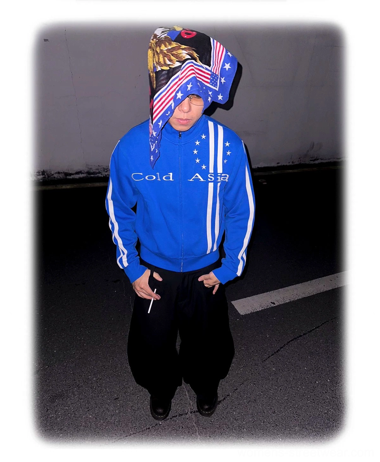 Blue starstripe track jacket worn with loose black trousers on a nighttime road, highlighting the cropped sporty fit and retro streetwear graphics