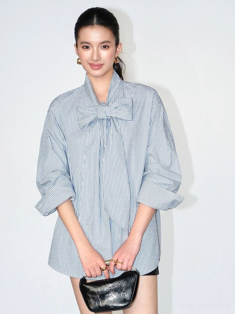 Asian model styling a blue and white vertical striped bow blouse with rolled cuffs, relaxed fit, straight hem, and black clutch