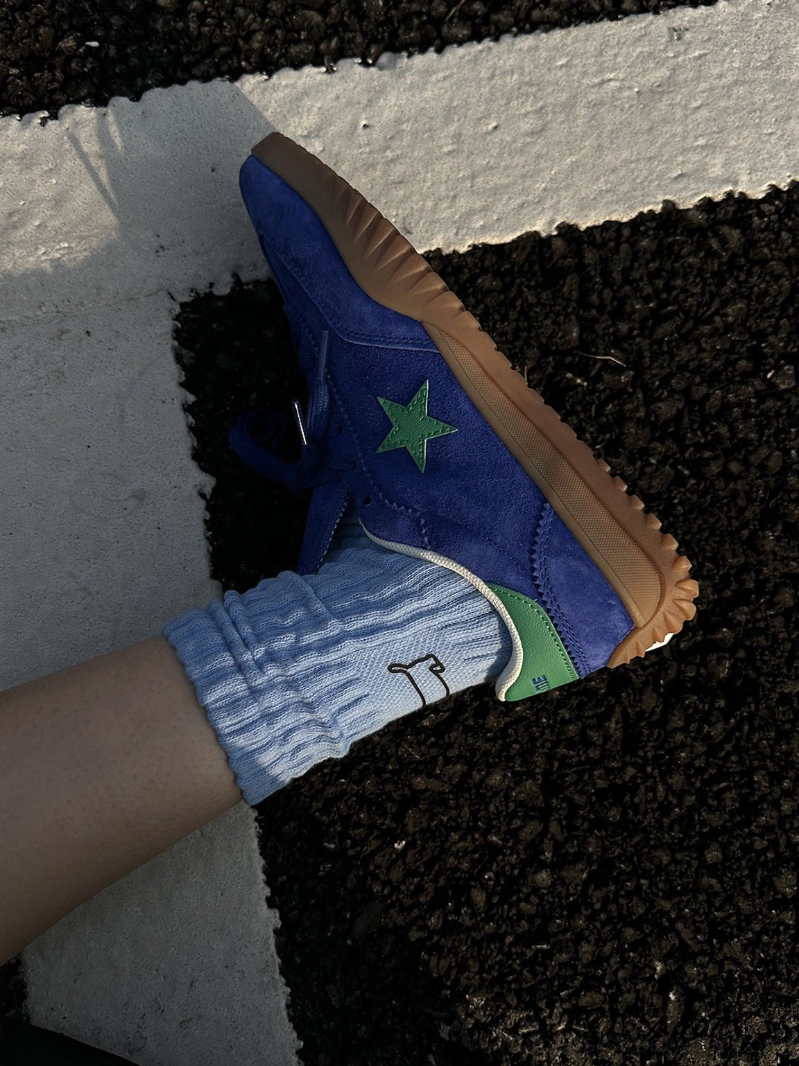 Top view close-up of blue suede star embroidered sneaker with green logo and gum sole worn with light blue crew sock