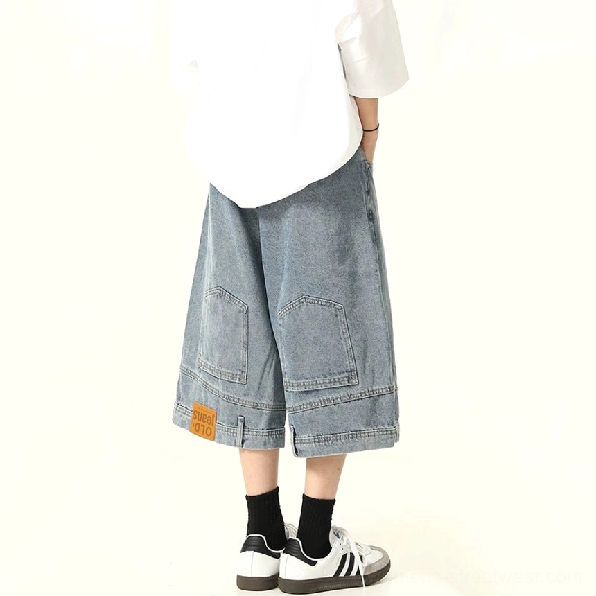 Rear side view of blue washed wide-leg denim culotte shorts with utility cargo pockets, hem fabric tag, oversized white T-shirt, and retro sneakers