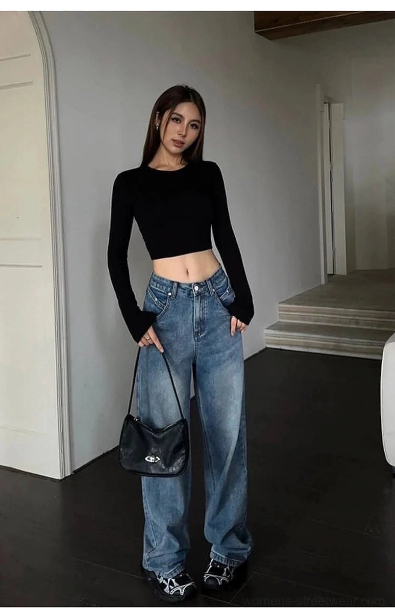 Full-body indoor styling of traditional blue washed loose wide-leg denim jeans with a black cropped long-sleeve top