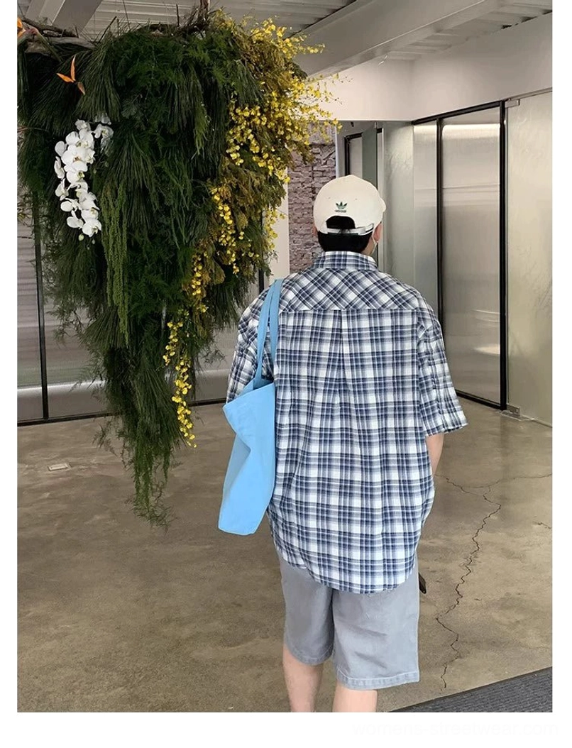 Full-body back view showing the classic blue and white grid plaid pattern across an oversized short sleeve shirt styled with a blue tote bag and casual streetwear accessories