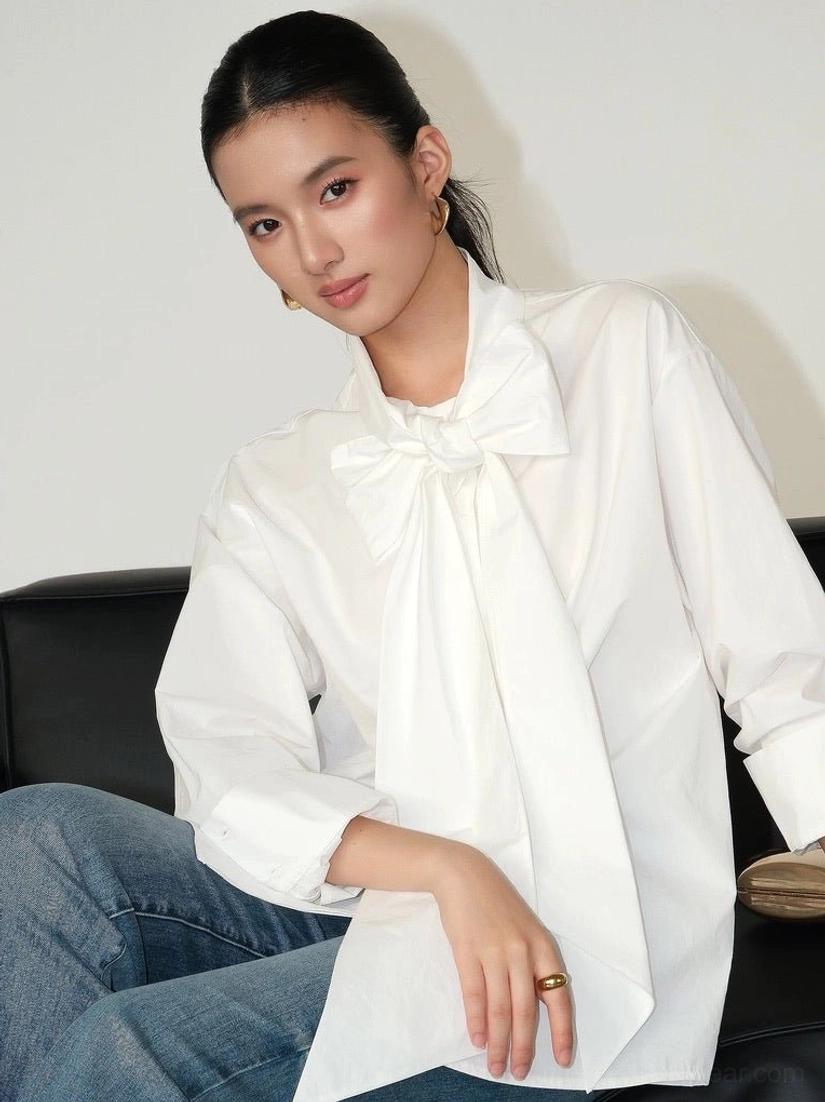 Side view of a blue and white striped oversized cotton blouse with large bow collar, rolled sleeves, and softly curved longer shirt hem