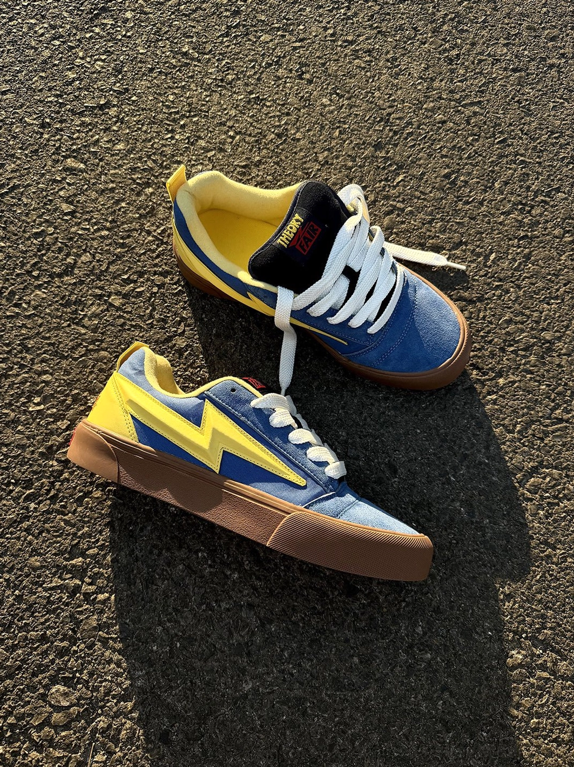 Blue yellow lightning bolt colorblock skate sneakers displayed as a pair on asphalt with white laces and gum soles