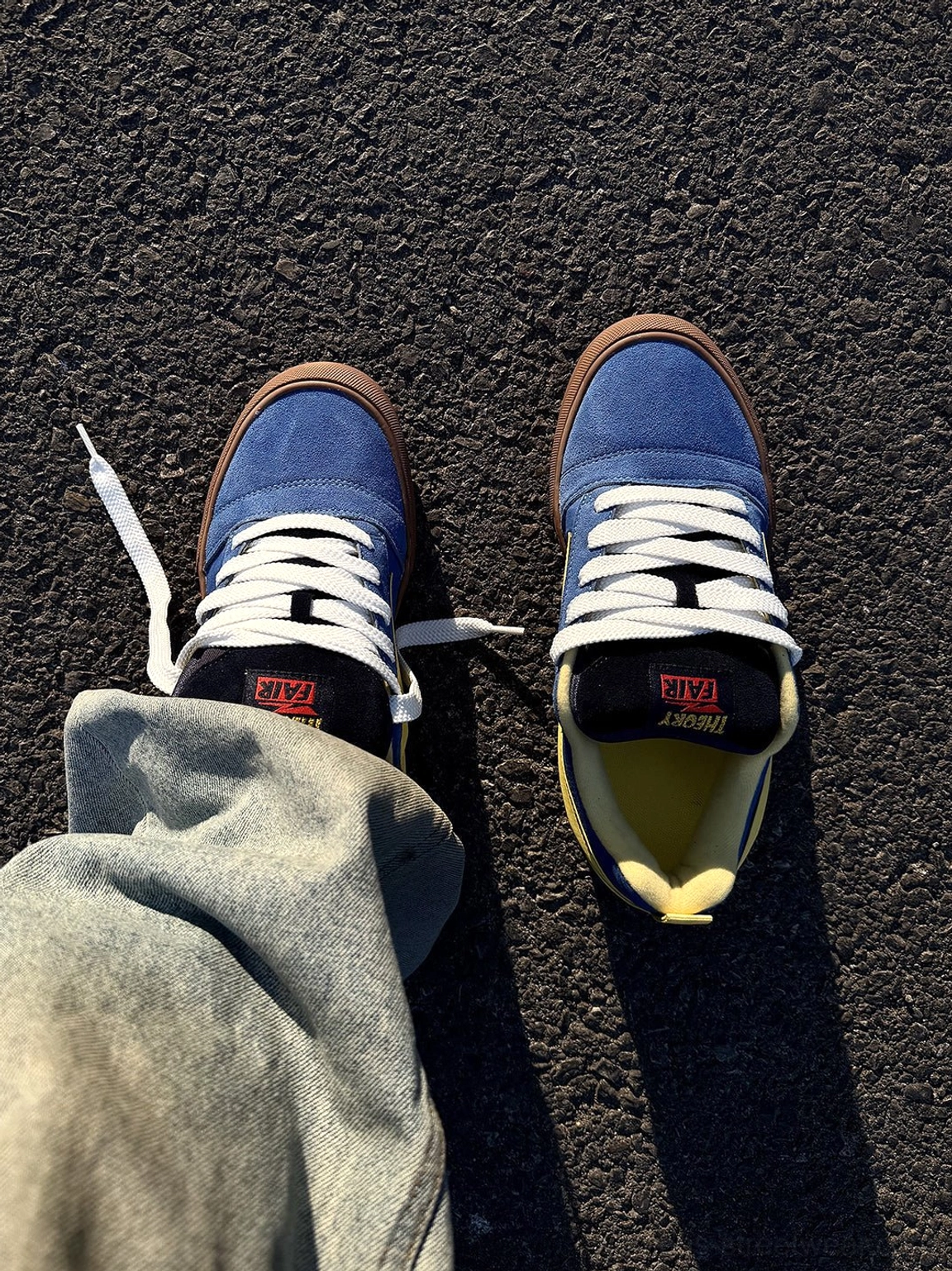 First person view of blue yellow lightning bolt colorblock skate sneakers worn with loose light wash denim pants