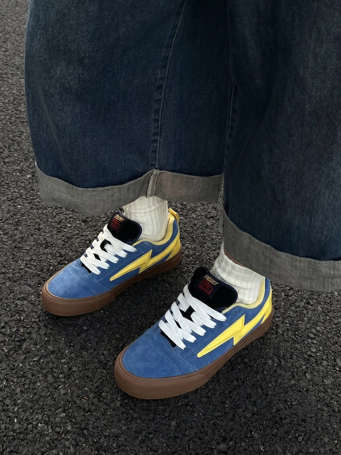 Overhead view of matching blue and yellow lightning bolt colorblock skate sneakers with white flat laces