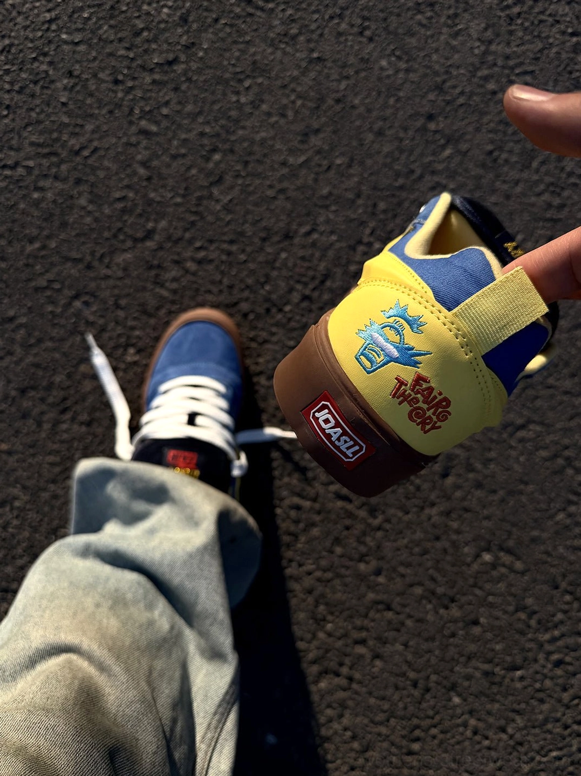 Hand held blue yellow lightning bolt skate sneaker showing graphic heel detail, yellow lining, and gum rubber outsole