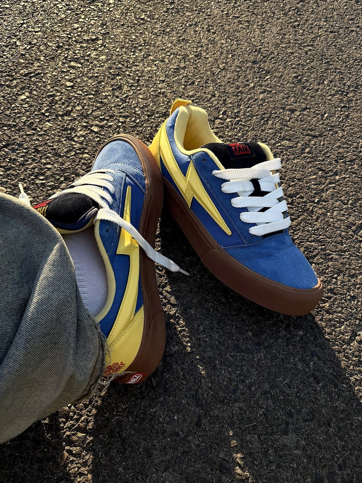 Top down view of blue and yellow lightning bolt skate sneakers with yellow inner lining worn with grey denim jeans