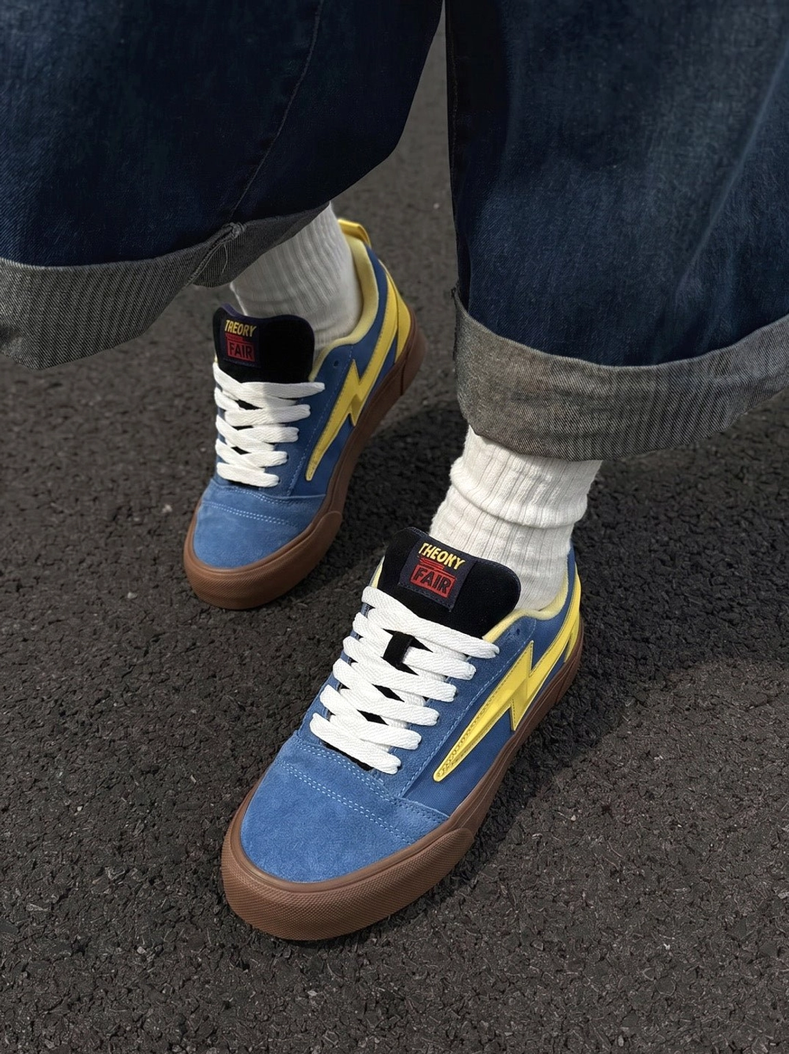 Blue yellow lightning bolt skate sneakers worn with rolled denim jeans and white crew socks in a streetwear outfit