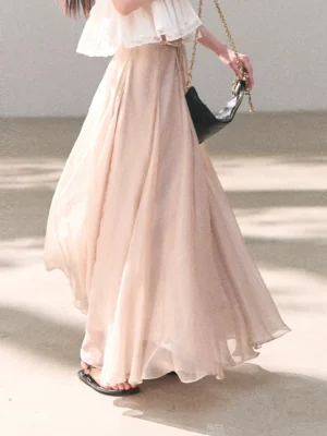 Blush chiffon A-line maxi skirt in a sunlit studio, showing the floor-length flowing panel silhouette