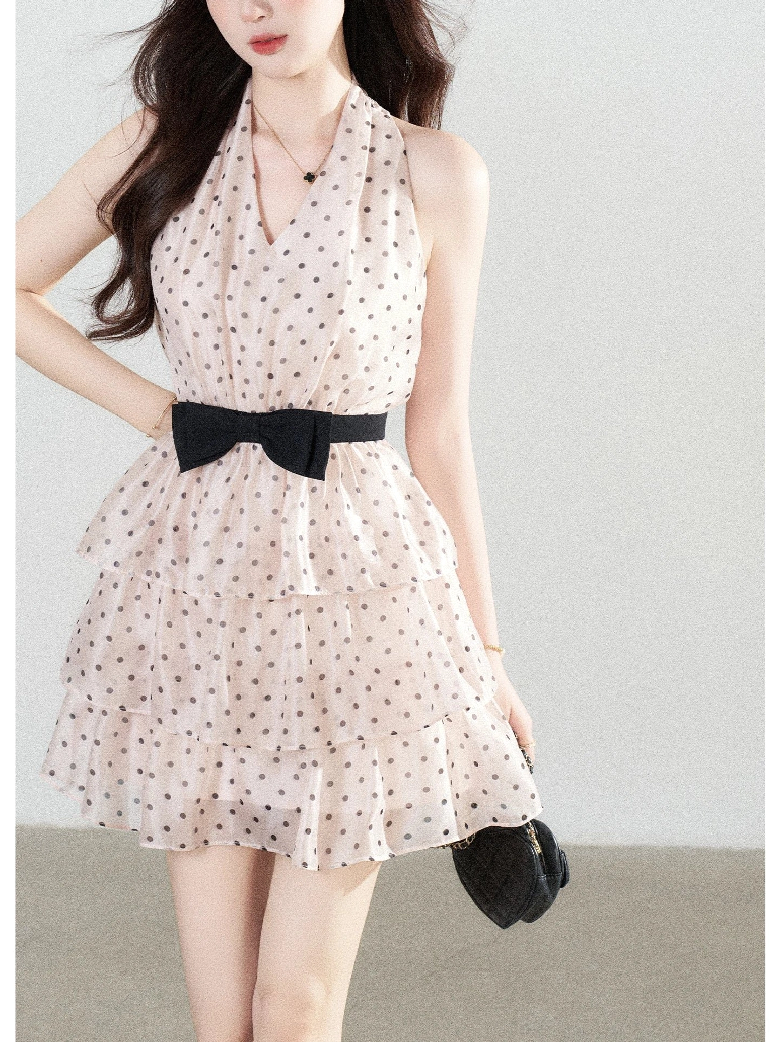 Blush pink polka dot halter mini dress close front view showing black bow waistband and tiered ruffle skirt