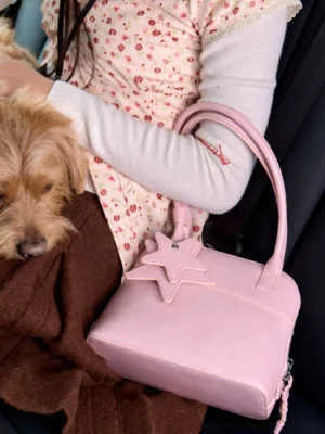 Blush pink star charm mini bowling handbag with top handles shown on a model's arm inside a car