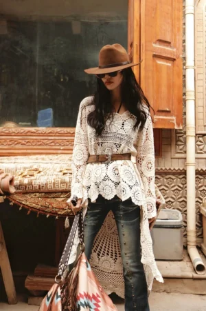 Model wearing a beige apricot boho crochet lace high-low tunic with jeans, cowboy hat, sunglasses, leather belt, cowboy boots, and geometric tote on an old town street