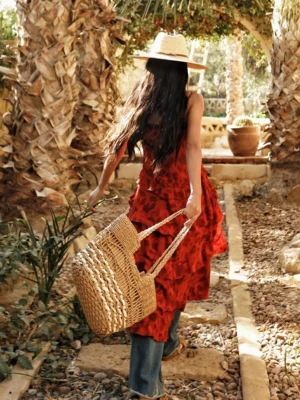 Red floral boho ruffle high-low camisole top shown from the back with a flowing asymmetric hem, wide-leg jeans, straw hat, and woven tote in a Mediterranean palm courtyard