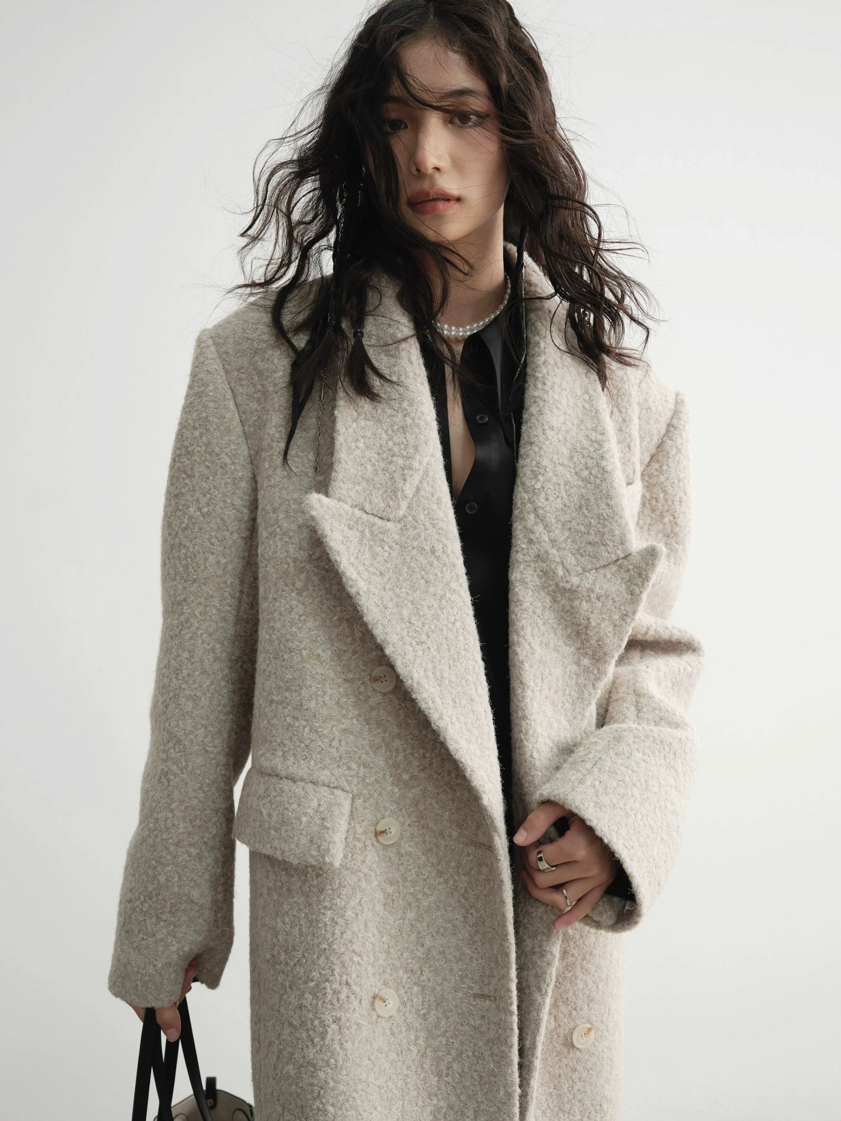 Close-up of soft bouclé wool coat texture with tailored lapels, double-breasted button details and pearl necklace styling