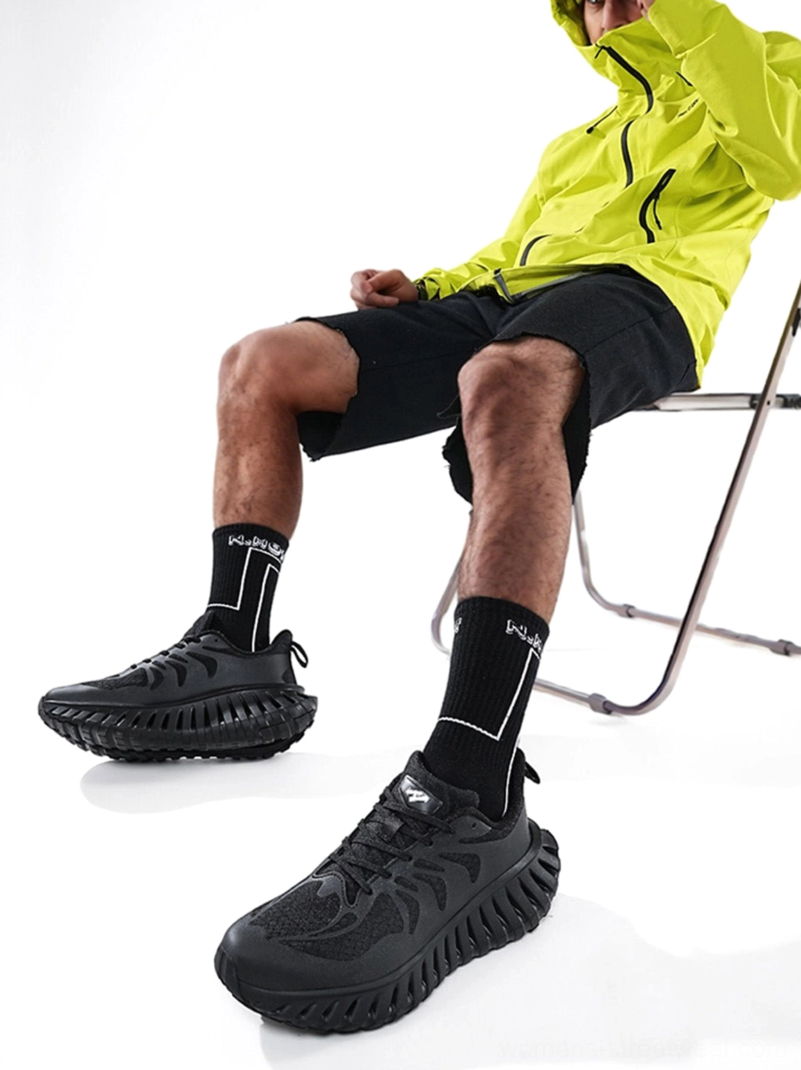Black low-top running sneakers shown on a seated model with a textured paneled upper and thick traction-inspired outsole