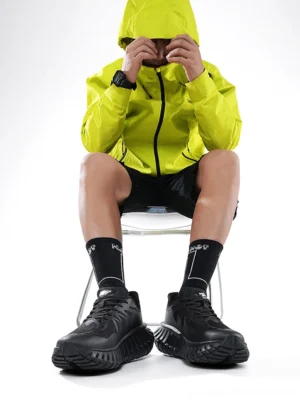 Black running sneakers worn with an outdoor streetwear outfit, showing the breathable athletic upper, cushioned profile, and rugged serrated outsole