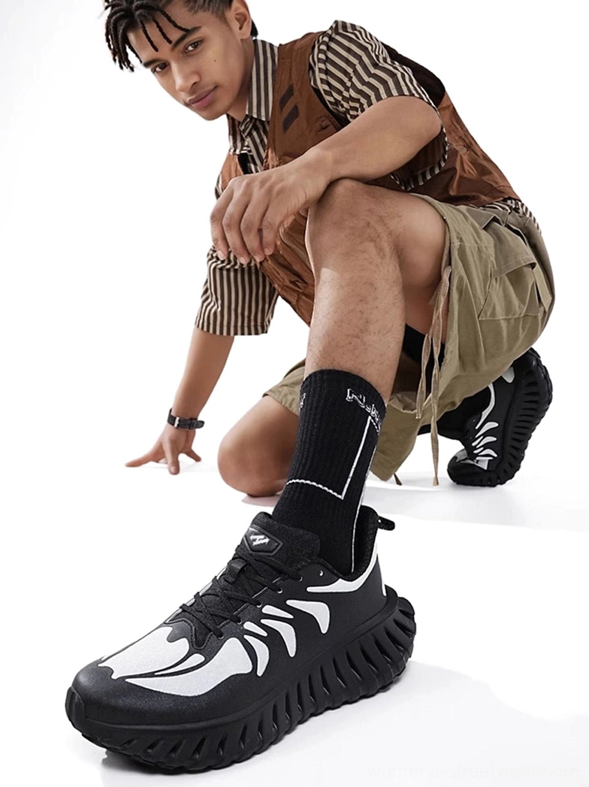 Black and white breathable running sneakers worn with a casual utility outfit, clearly displaying the graphic skeletal upper pattern