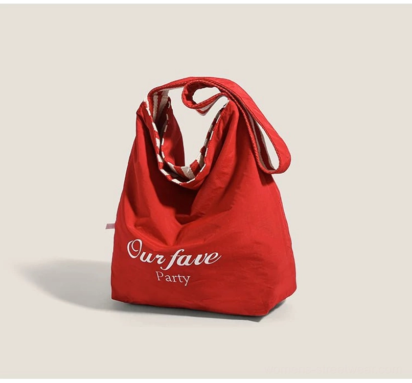 Bright red canvas hobo shoulder bag with embroidered lettering, wide curved strap, and relaxed open-top shape