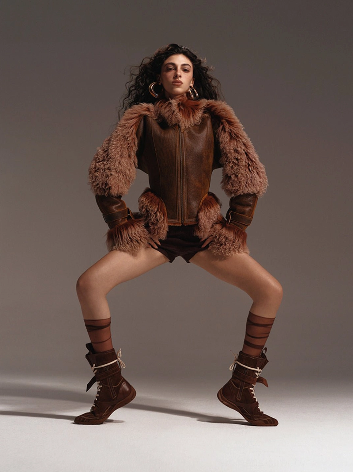 Brown asymmetric foldover mid-calf utility boots styled with a fur-trimmed leather outfit and striped socks in an avant-garde streetwear look