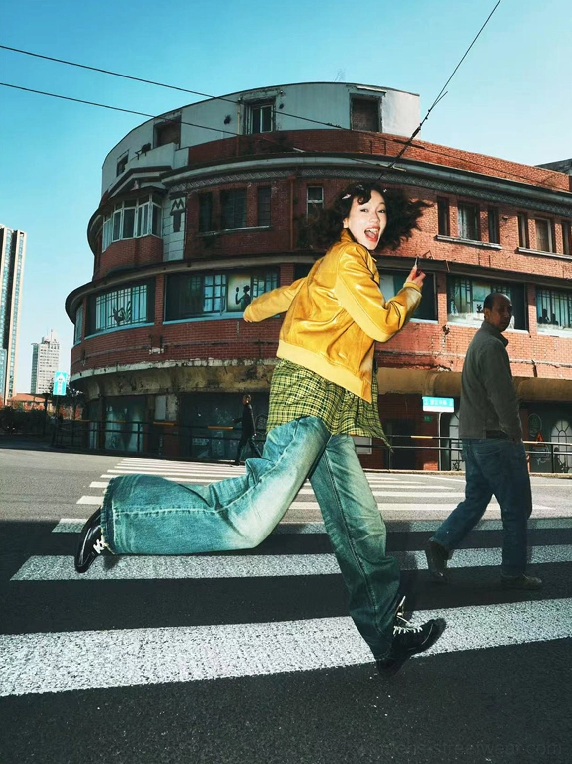 Brown asymmetric lace-up mid-calf utility boots styled with a yellow jacket and blue jeans in a dynamic urban streetwear outfit
