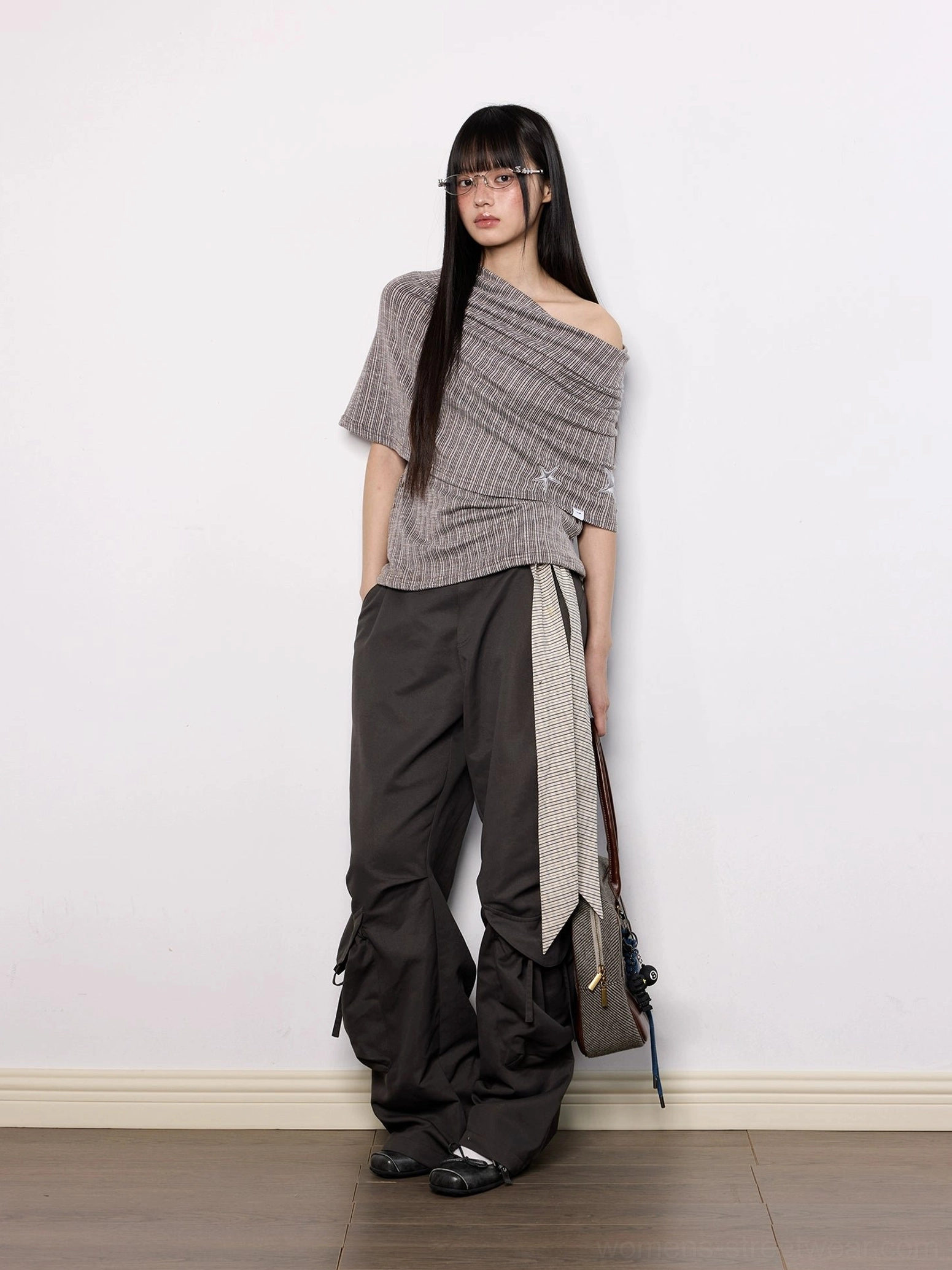 Side view of brown off-shoulder pinstripe knit top with draped asymmetric collar, embroidered star detail, and fitted Acubi silhouette