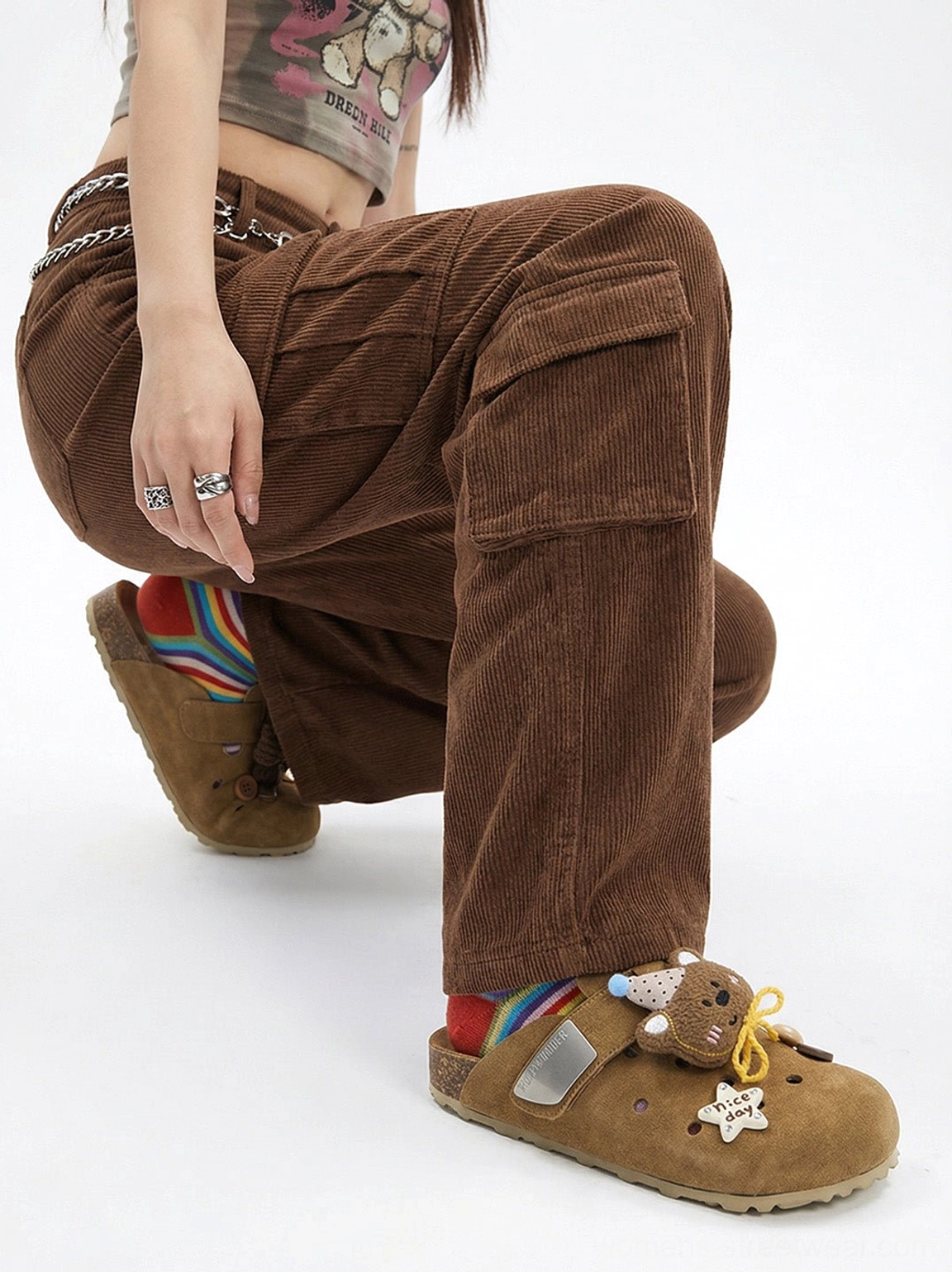 Side view of model wearing a brown bear and star charm clog with corduroy cargo pants, rainbow socks, and earth-tone streetwear layers
