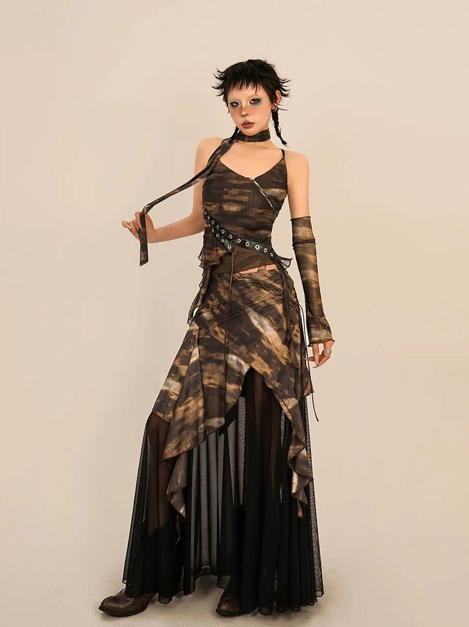 Full body front view of a brown and black abstract tie dye asymmetrical mesh skirt and camisole streetwear set with layered ruffled hem grommet waist belt sheer sleeves and matching arm accessories