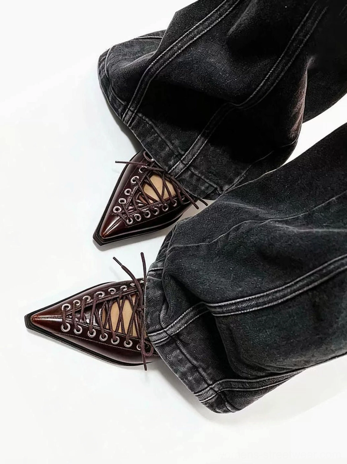 Brown corset-lace pointed heel pumps worn with dark wash baggy denim jeans, showing the polished lace-up vamp and metal eyelet details