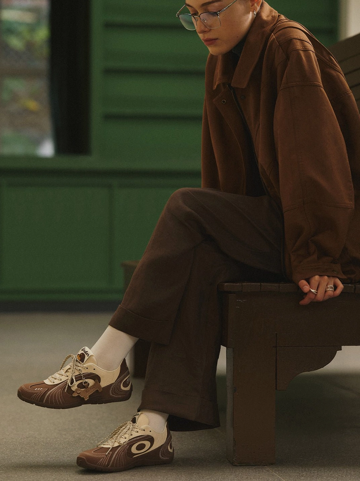 Brown and cream dog charm retro trainers styled with a brown coordinated outfit against a vintage green wall