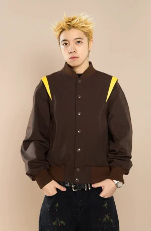 Male model wearing brown crown embroidered baseball jacket with dark graphic jeans in a full body streetwear outfit