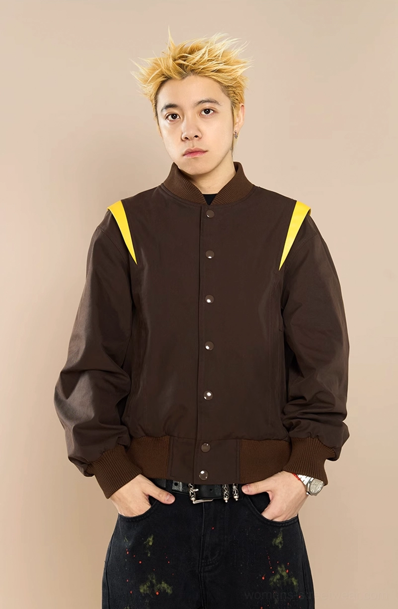 Male model wearing brown crown embroidered baseball jacket with dark graphic jeans in a full body streetwear outfit