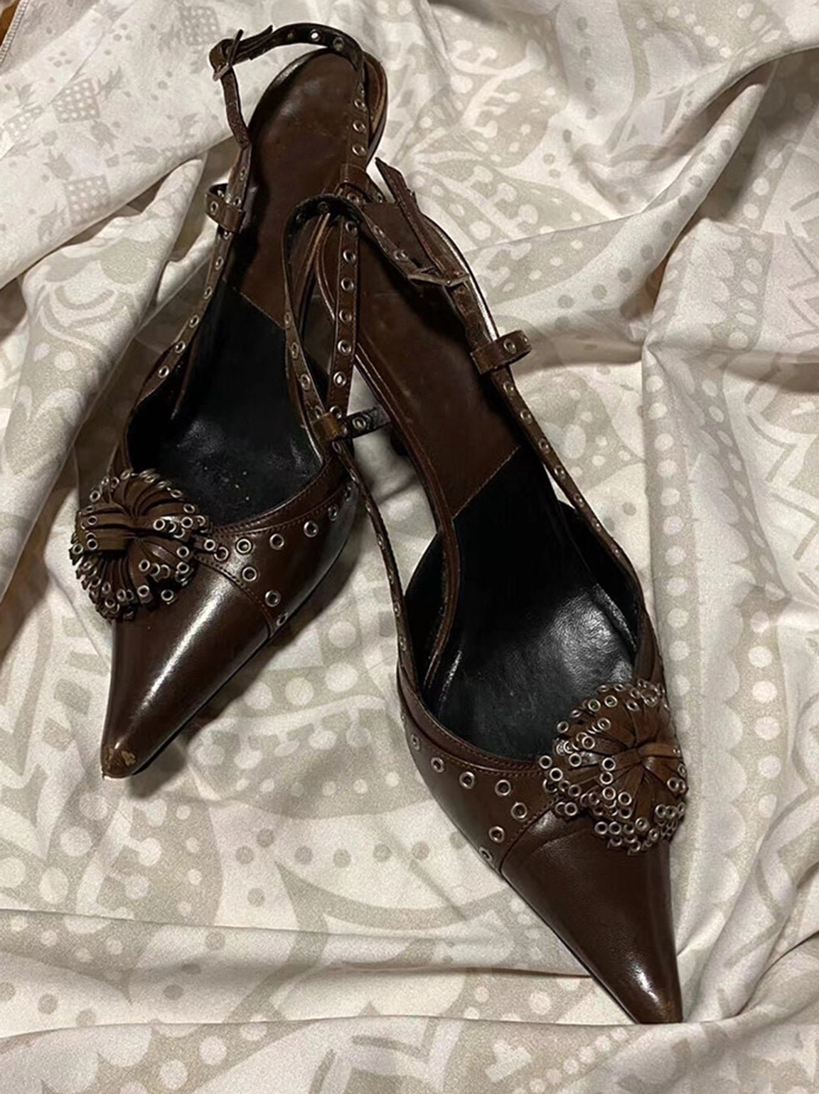 Brown crystal stud pointed slingback heels shown from an oblique side angle with rivet trim, sharp pointed toe, and adjustable slingback ankle strap