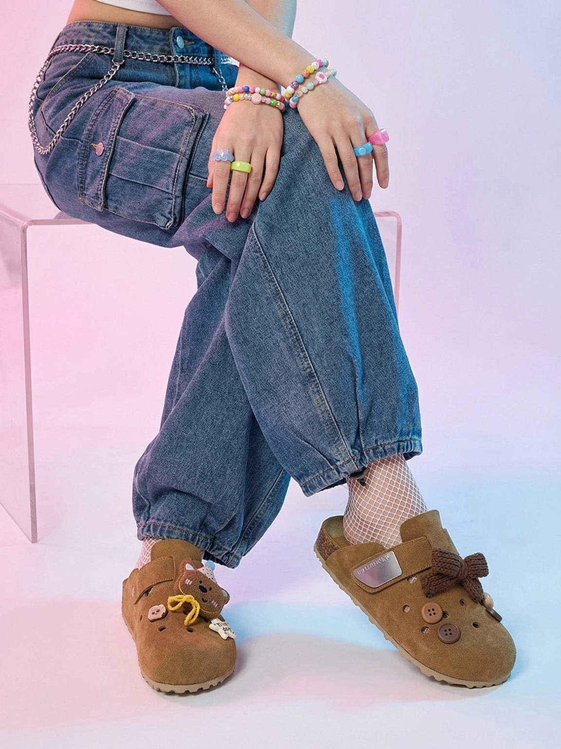 Model seated in baggy blue denim cargo pants wearing brown decorative perforated clogs in a colorful Y2K streetwear outfit