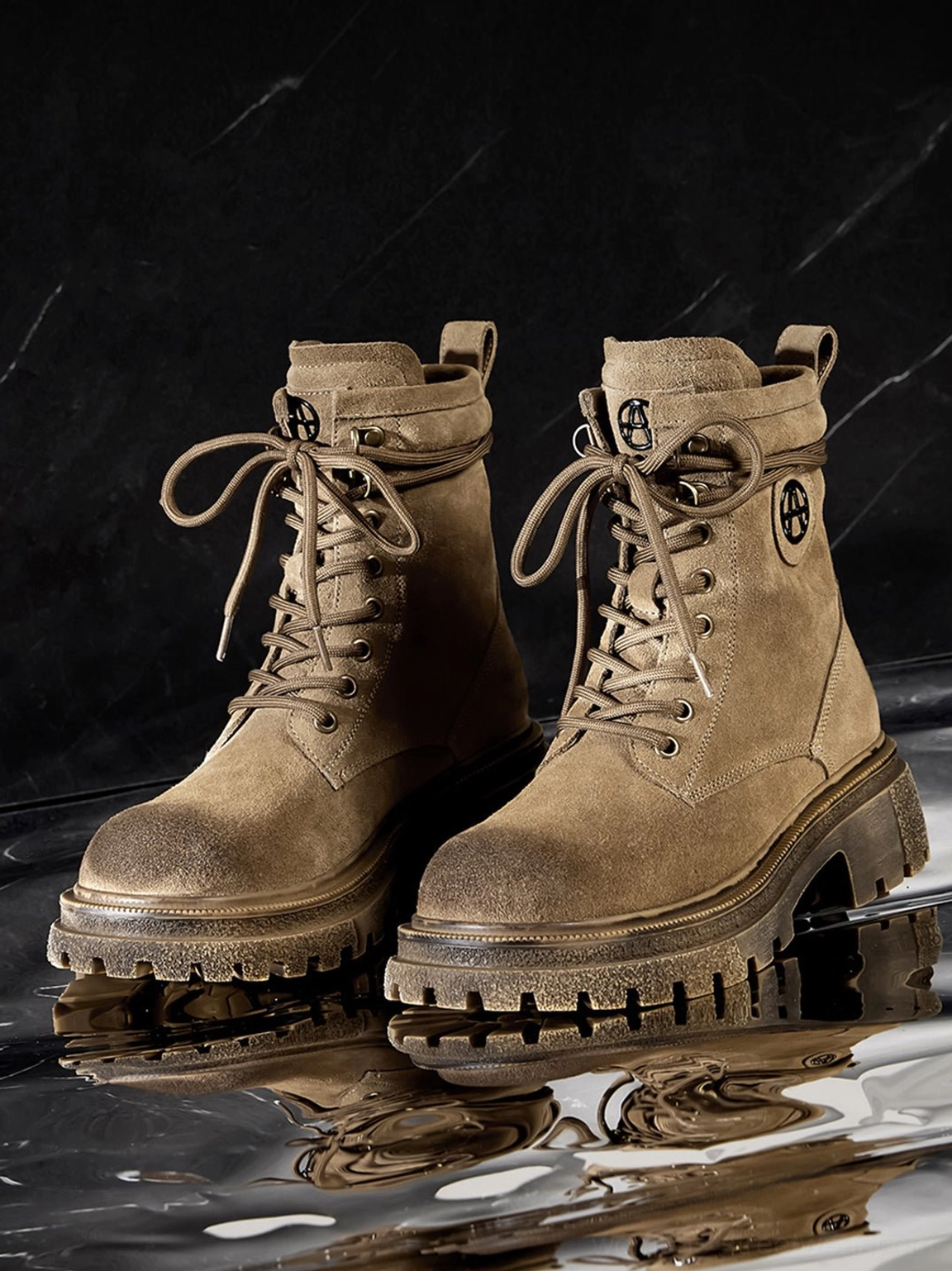 Pair of brown distressed suede combat boots front view on dark marble water reflection background showing logo details