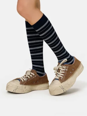 Brown distressed platform sneakers styled with navy striped knee-high socks in a vintage streetwear outfit