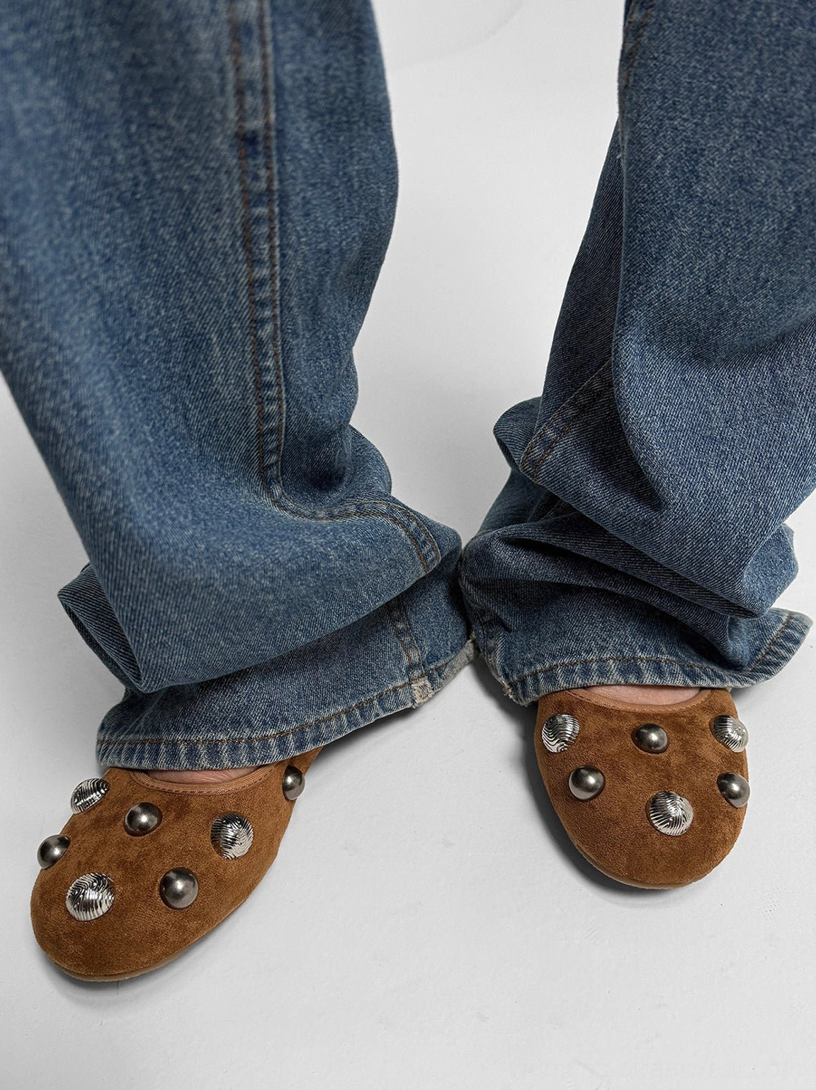 Pair of brown embellished ballet flats worn with blue wide-leg denim jeans in a relaxed streetwear outfit
