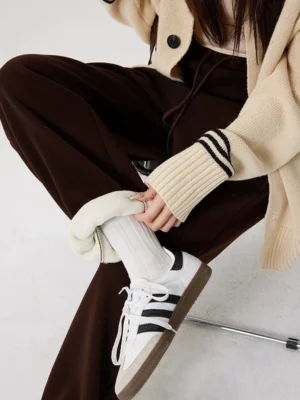Close-up of brown fleece-lined streetwear sweatpants with the cuff folded to reveal the soft plush lining, styled with ribbed socks and striped sneakers