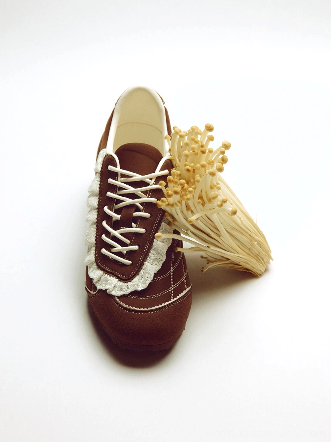 Brown frilled low-profile sneaker viewed from above showing the ruffled lace overlay white lacing system and rounded toe