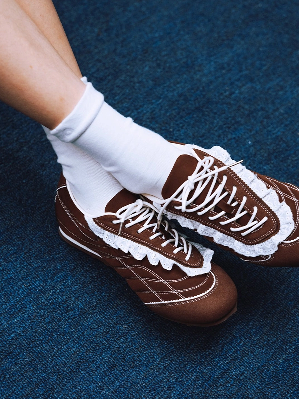 Side view of brown frilled low-profile sneakers worn with white socks showing the fitted retro athletic shape