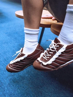 Pair of brown frilled retro trainer sneakers worn with white crew socks in a casual streetwear styling view